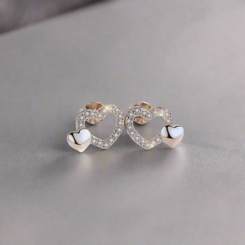 These earrings are elegant and delicate, crafted from 925 sterling silver. They feature a heart-shaped design adorned with shimmering zircon stones that enhance their sparkle. Each earring showcases two interconnected hearts, with the larger heart encrust